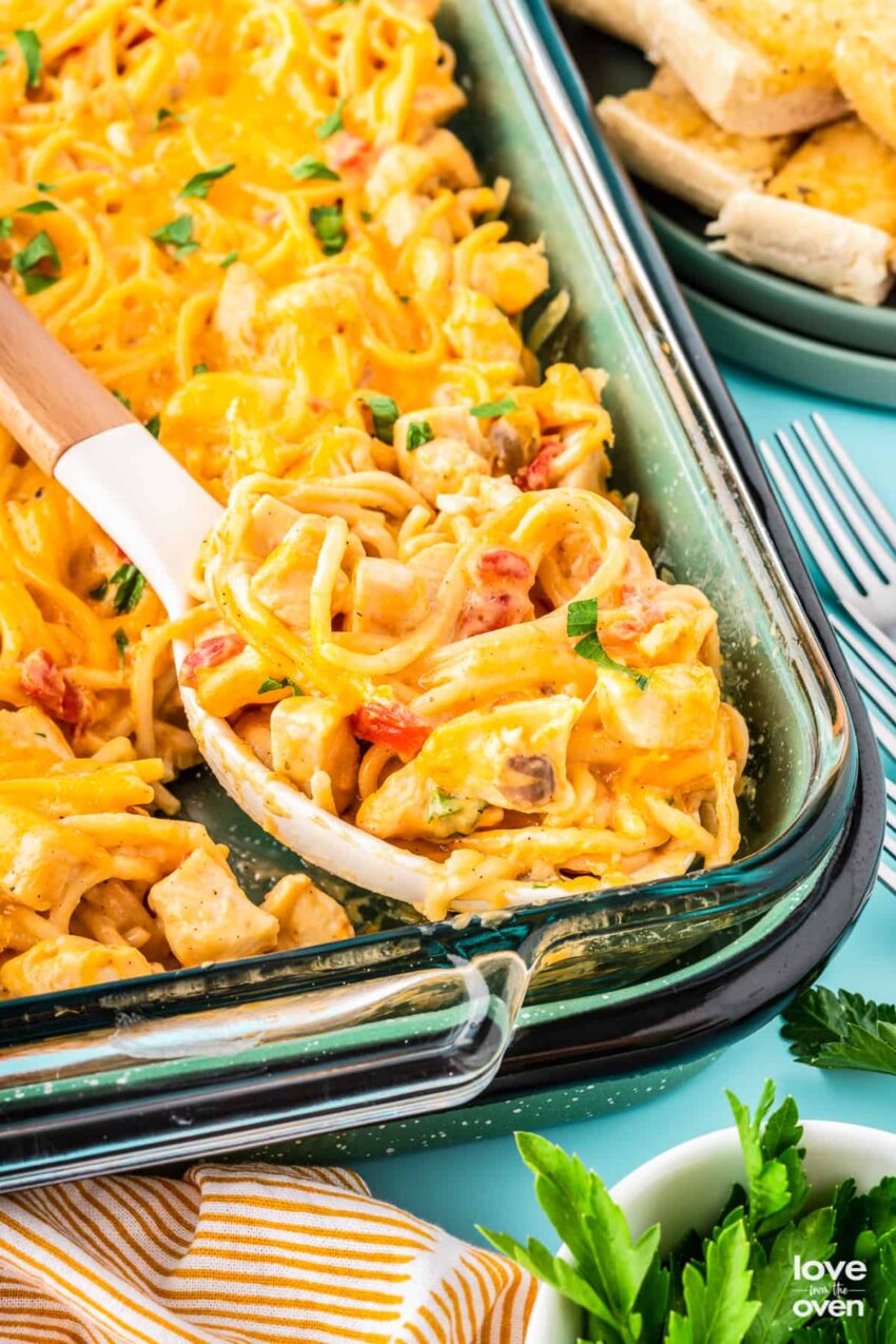 A delicious and creamy chicken spaghetti bake topped with melted mozzarella cheese, garnished with red pepper flakes and fresh parsley.