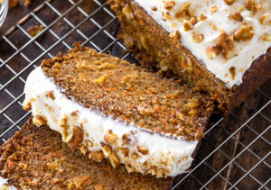 baked carrot cake loaf topped with creamy frosting and chopped walnuts on a wire rack.