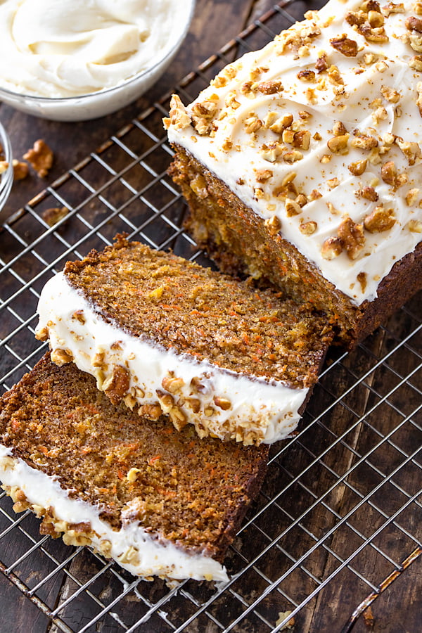 baked carrot cake loaf topped with creamy frosting and chopped walnuts on a wire rack.